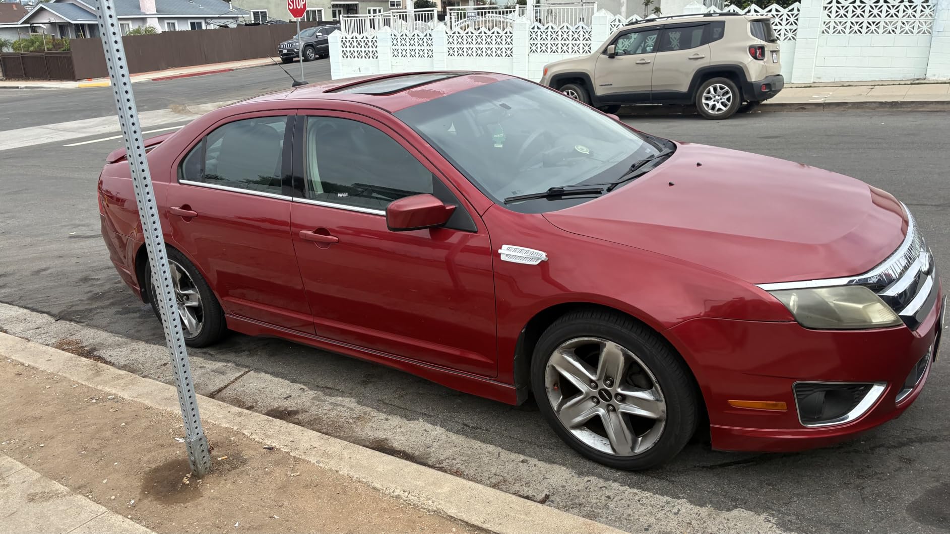 Red Ford Fusion parked at a curb with the coated paint throwing back the sky and the factory headlight lens still yellowed