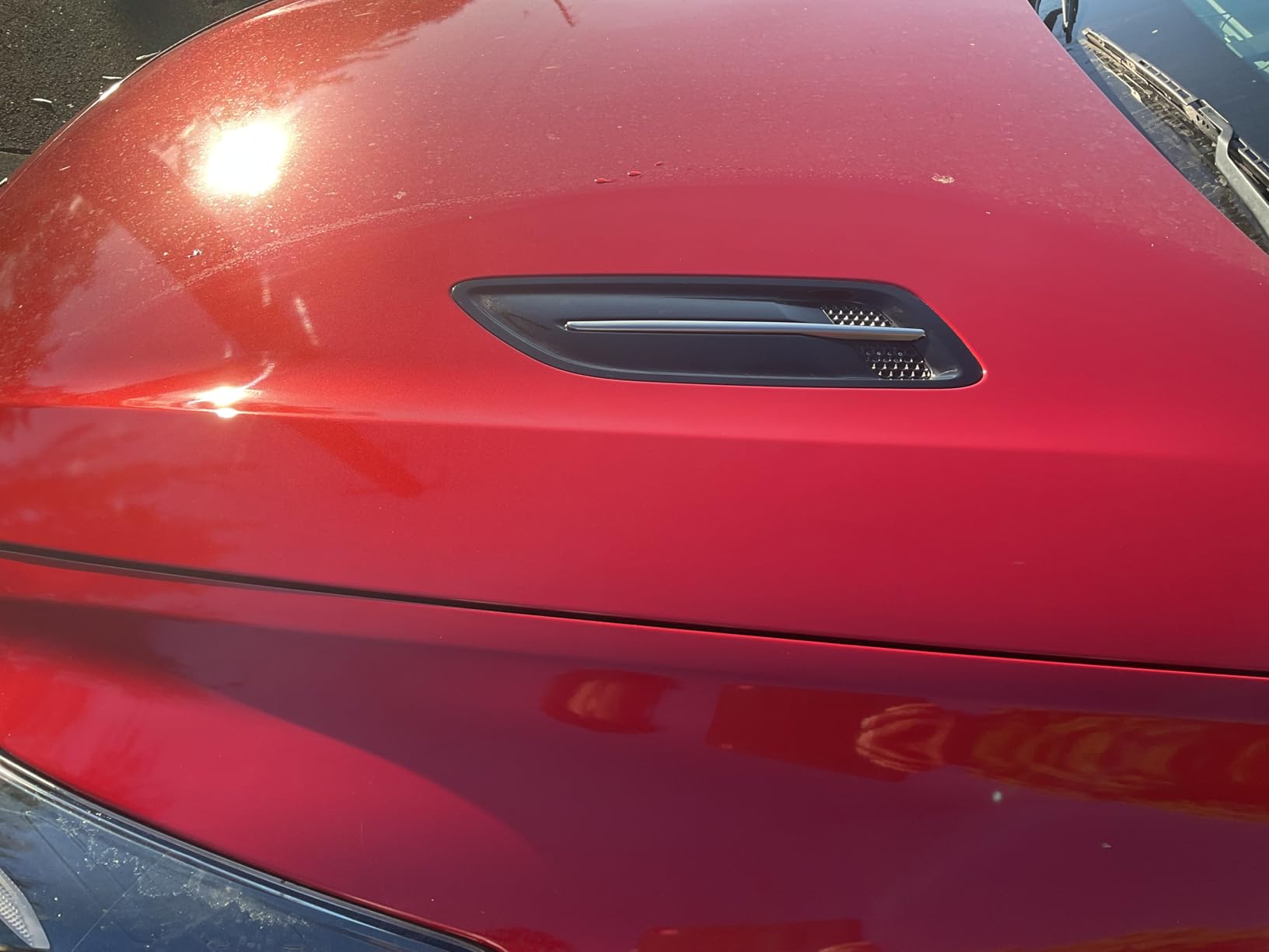 Close view of a red hood and fender vent, the coated paint holding a hard highlight from the sun