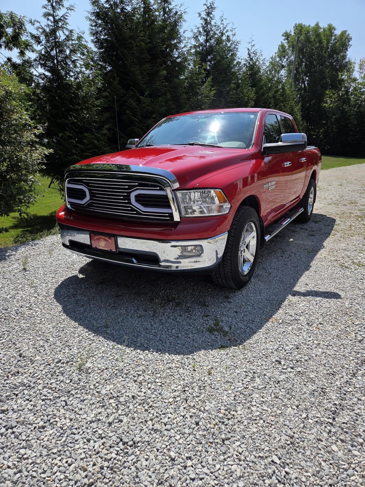 Red Ram 1500 crew cab on a gravel driveway with the coated hood and chrome grille under full sun