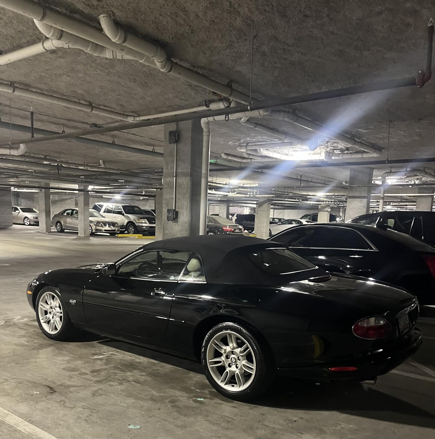 Black Jaguar XK convertible in a parking garage, picking up the overhead lights as clean streaks along its flanks